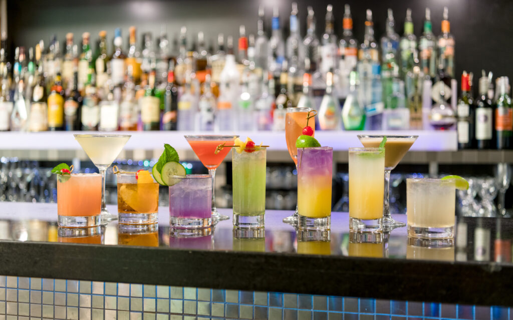 many colourful cocktails lined up at a bar